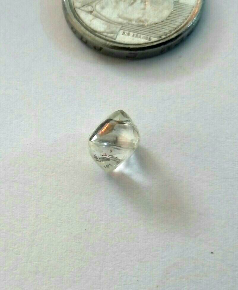 Foto de um diamante que pesa 2 gramas e mede aproximadamente 5 milímetros. Foto próximo de uma moeda de 50 centavos para comparação de tamanho. Uma das Grandes Fortunas Inestimáveis